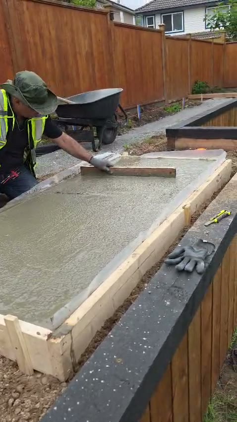 Screeding a freshly poured concrete pad inside timber formwork