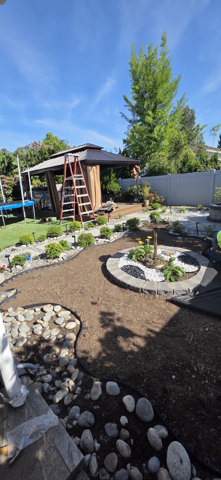 Landscaped backyard with gazebo, stone planter and river-rock borders