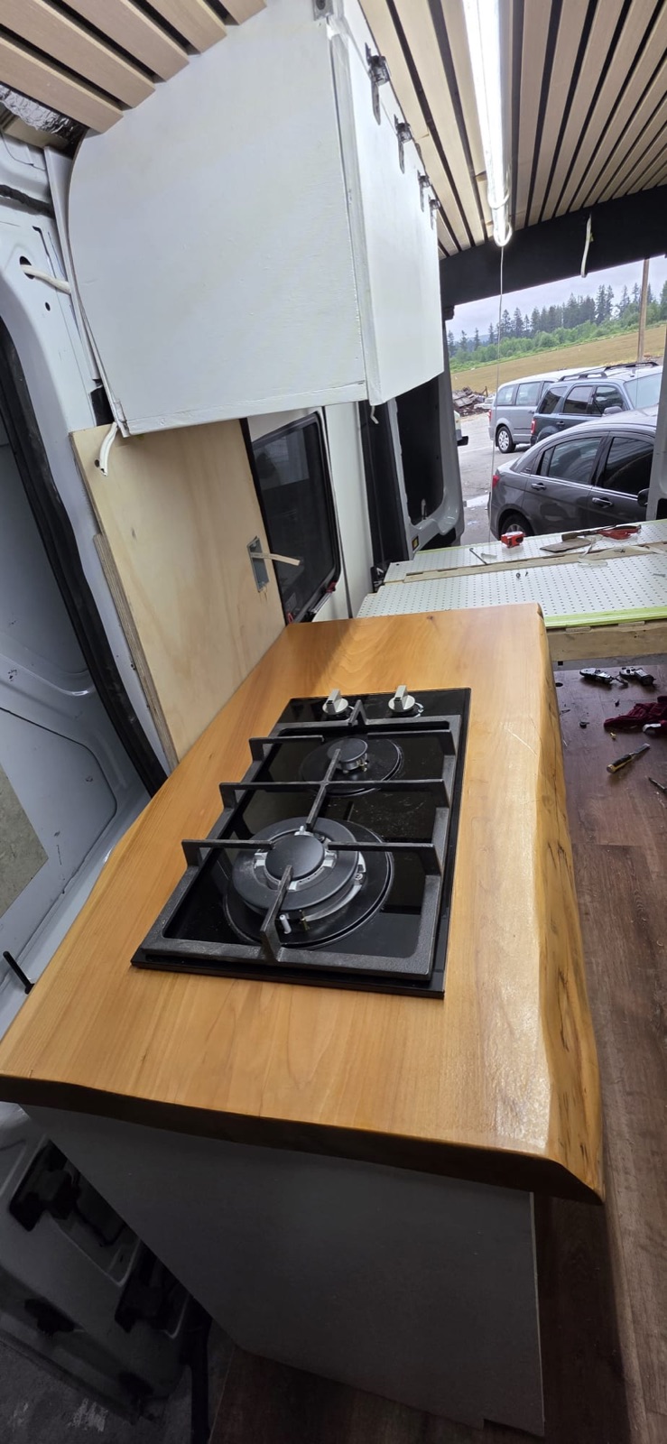 Finished camper van conversion with live-edge galley and gas cooktop
